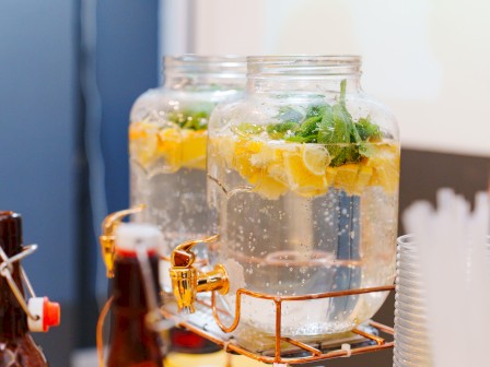 Glass jars filled with lemon and mint-infused water, set on a rustic stand near soda bottles and plastic cups.