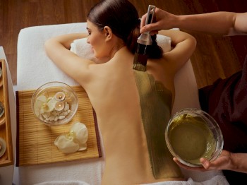 A woman is receiving a green clay or mud treatment on her back at a spa, with candles and spa items nearby, ending the sentence.