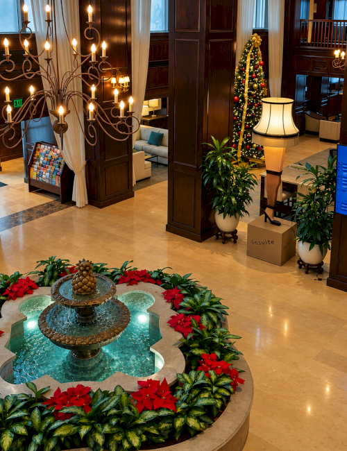 This is a hotel lobby decorated for Christmas with poinsettias, a fountain, a Christmas tree, and elegant lighting and furniture.