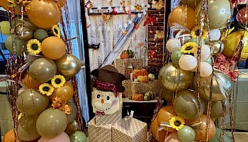 Fall-themed party decor with balloons, a pumpkin, sunflower accents, and a cheerful snowman figure.