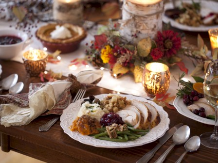 A festive table set with roasted turkey, mashed potatoes, green beans, cranberry sauce, and holiday decorations.