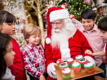 Santa is giving cupcakes to children during a Christmas celebration.
