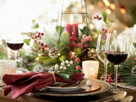 A festive table setting with wine glasses, candles, greenery, red berries, and decorations for a holiday celebration.