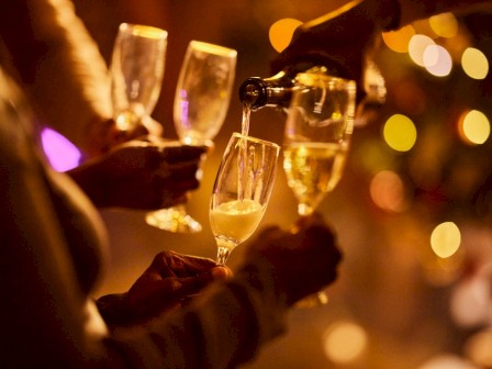 People celebrating with champagne at a festive gathering, pouring drinks, in a warm, bokeh-lit setting.