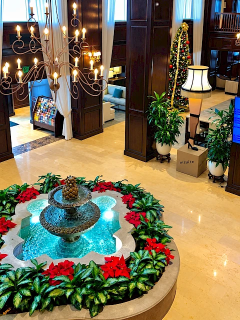 This is an elegant hotel lobby decorated for Christmas with a fountain, poinsettias, a Christmas tree, and warm lighting.