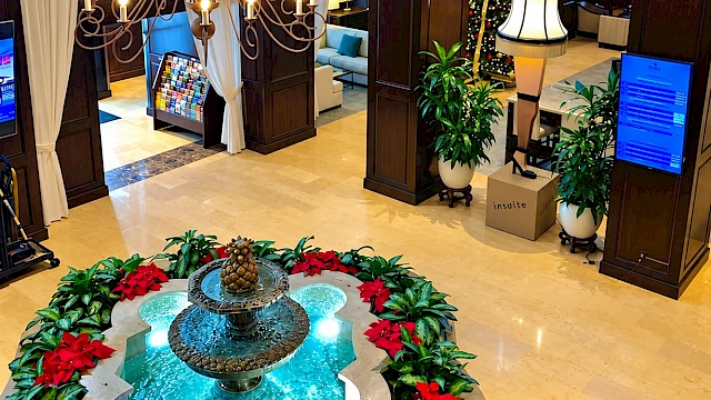 This is an elegant hotel lobby decorated for Christmas with a fountain, poinsettias, a Christmas tree, and warm lighting.