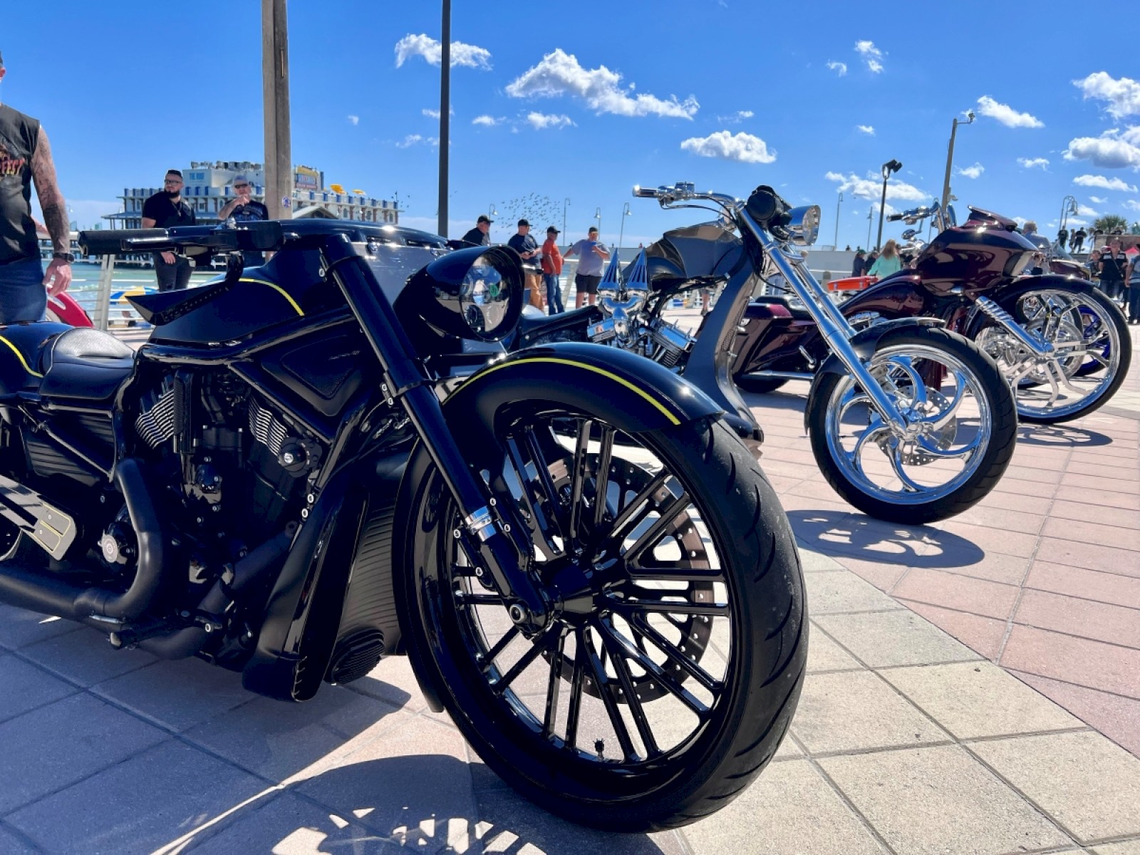 Black custom motorcycles with shiny chrome details are displayed outdoors on a sunny day at a bike event.