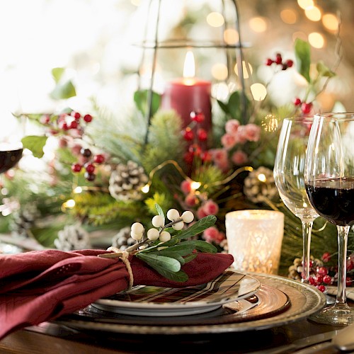 A beautifully set Christmas dinner table with red wine glasses, festive decorations, candles, and greenery.