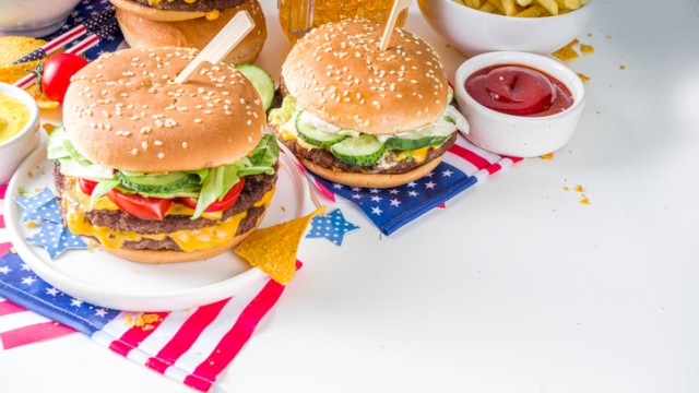 Two cheeseburgers with lettuce, tomato, and pickles on a patriotic-themed table, accompanied by fries and ketchup.