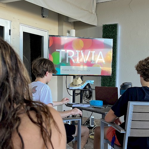 People are seated indoors, facing a screen displaying 