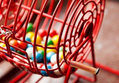 A close-up of a red metal bingo cage filled with colorful bingo balls, showing a handle for rotating the cage.