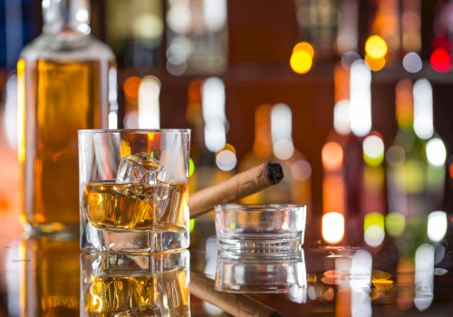 A glass of whiskey with ice, a cigar in an ashtray, and a bottle, set against a blurred background of colorful lights.