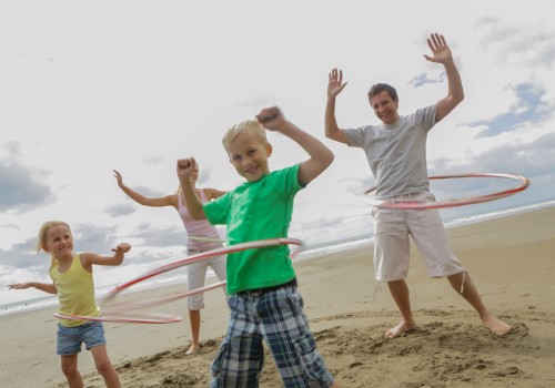 A family is having fun on the beach, hula hooping and smiling, with the ocean and cloudy sky in the background.