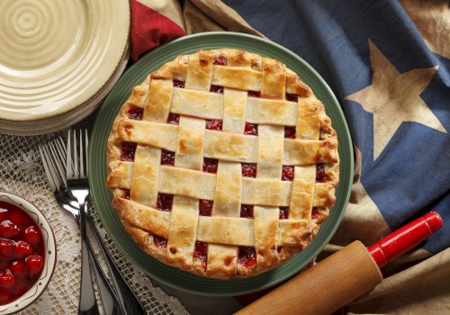 A cherry pie with a lattice crust on a green plate, surrounded by a Texas flag, utensils, a rolling pin, and a bowl of cherries ends the sentence.