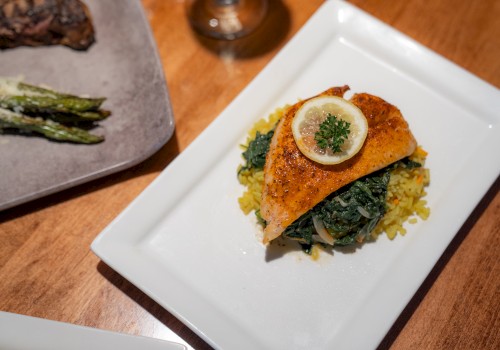 A plated dish featuring a piece of fish garnished with a lemon slice and parsley, served on a bed of spinach and yellow rice, alongside asparagus.