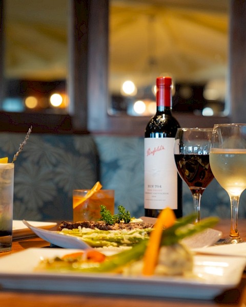 An elegant dinner setup featuring dishes, a bottle of wine, cocktails, and a glass of white wine on a wooden table.