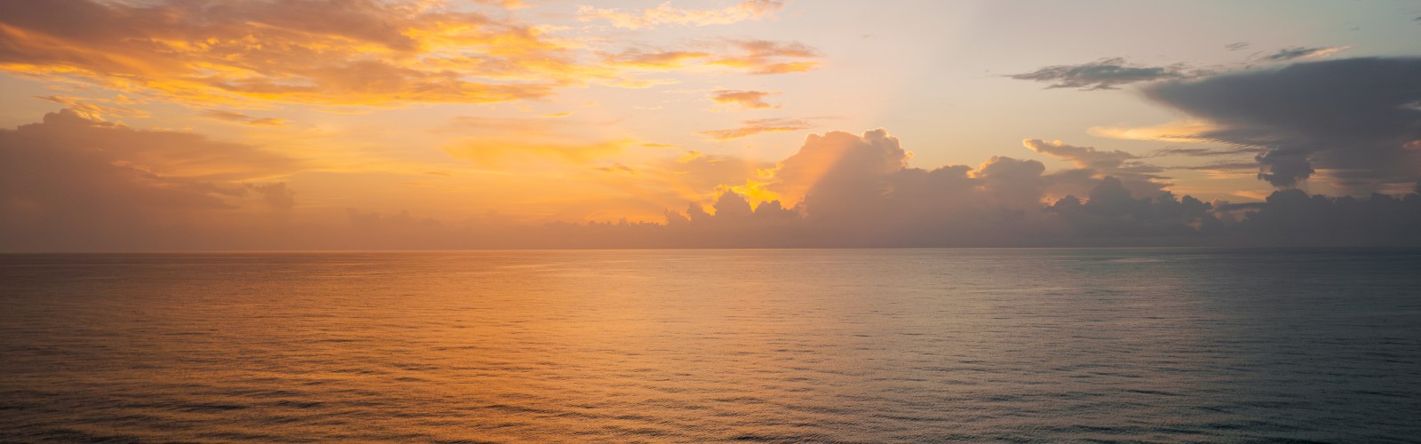 The image shows a serene ocean view at sunset, with a mix of orange, yellow, and dark clouds in the sky, reflecting on the calm waters.