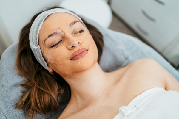 A person is lying down with a facial mask on, covered by a headband, appearing relaxed, possibly at a spa or during a beauty treatment.