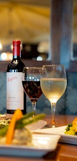 The image shows a table set for dining with various dishes, a bottle of red wine, and three glasses of different drinks.