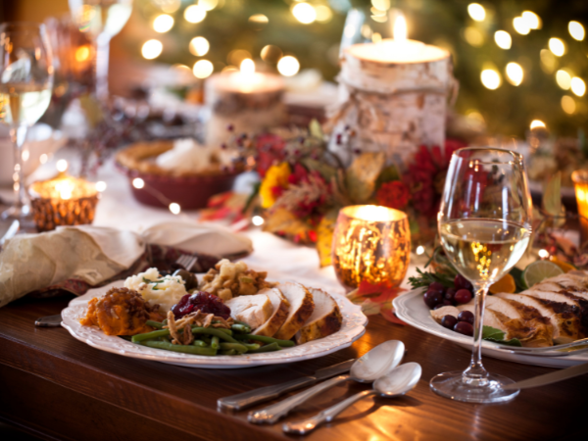 A festive dining table with candles, wine glasses, and plates of turkey, vegetables, and side dishes, set for a holiday meal.