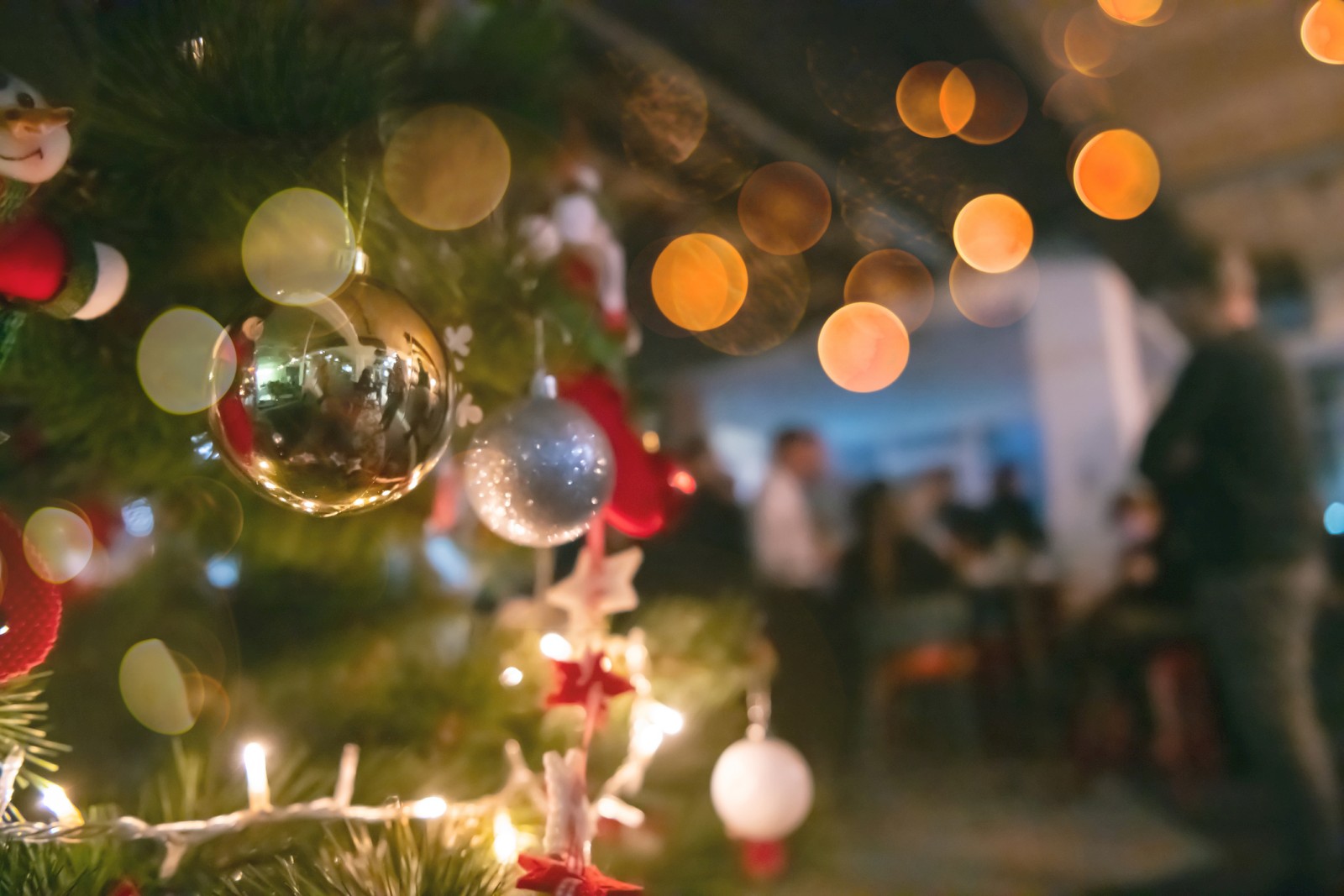 Christmas decorated tree with ornaments and lights, festive atmosphere, and blurred people in the background.