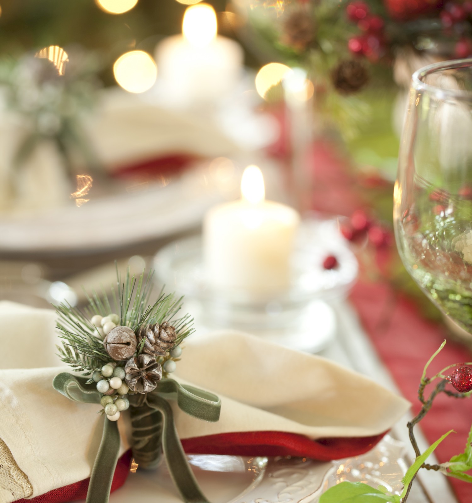 A festive table setting with plates, a napkin decorated with pinecones, candles, and blurred holiday lights in the background.