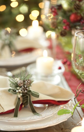 A festive table setting with plates, a napkin decorated with pinecones, candles, and blurred holiday lights in the background.