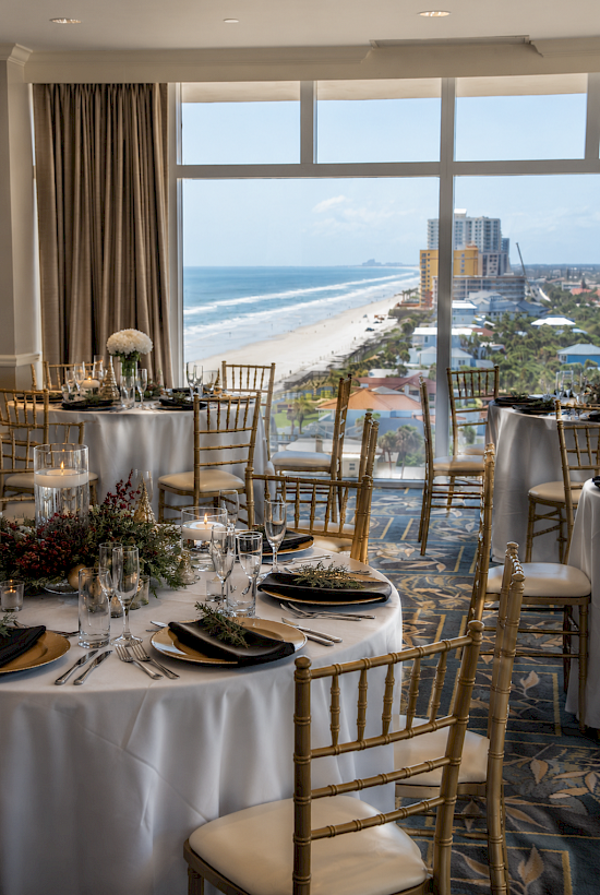 Elegant banquet setup with gold chairs, black napkins, and a beach view for a special celebration or event.
