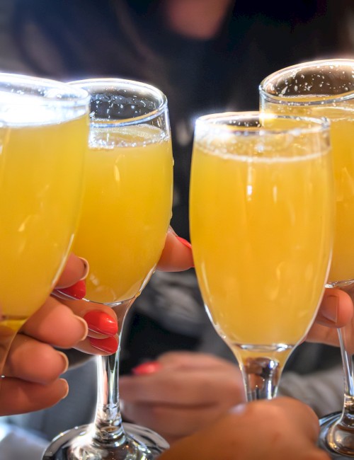 Four people toast with glasses of orange juice or mimosas in a celebratory setting.