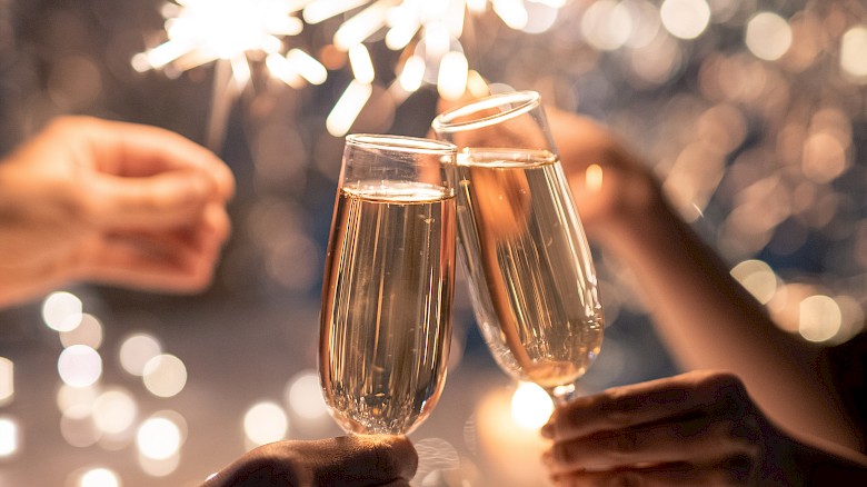 People clinking champagne glasses with sparklers in the background, surrounded by festive lights, creating a celebratory atmosphere.