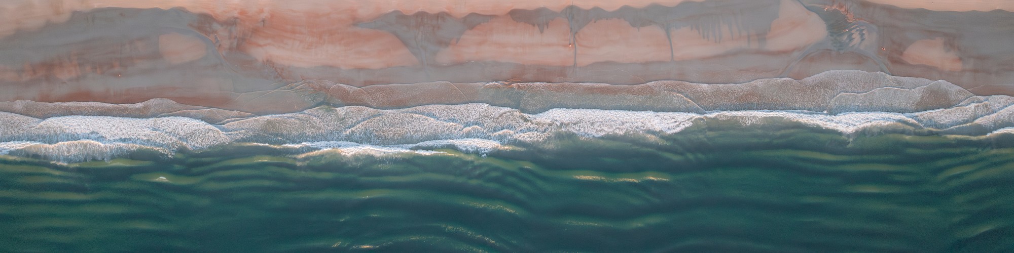 Aerial view of a beachfront neighborhood with houses, a road, sandy beach, and ocean waves hitting the shore.