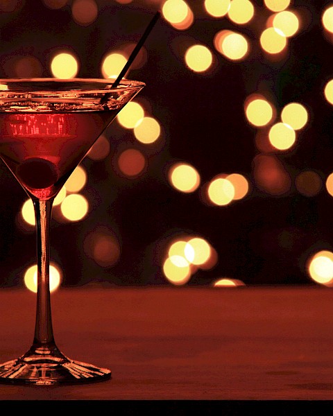 A martini glass with a cherry inside, against a backdrop of warm, bokeh lights.