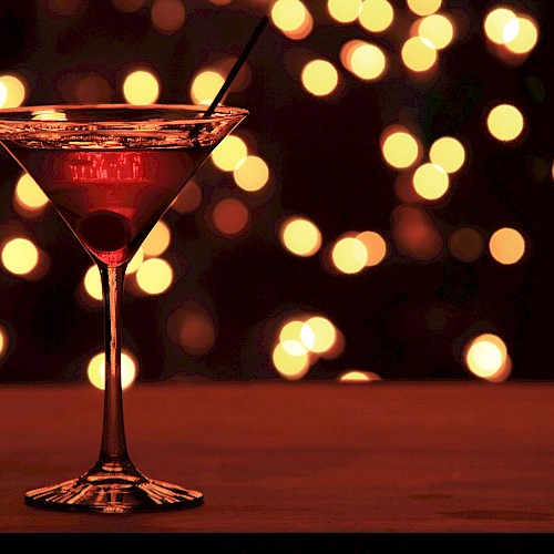 A martini glass with a cherry inside, against a backdrop of warm, bokeh lights.