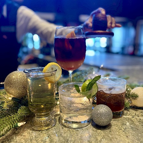 A selection of festive drinks with garnishes on a bar, surrounded by decorative ornaments and greenery.