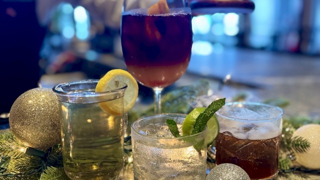 A selection of festive drinks with garnishes on a bar, surrounded by decorative ornaments and greenery.