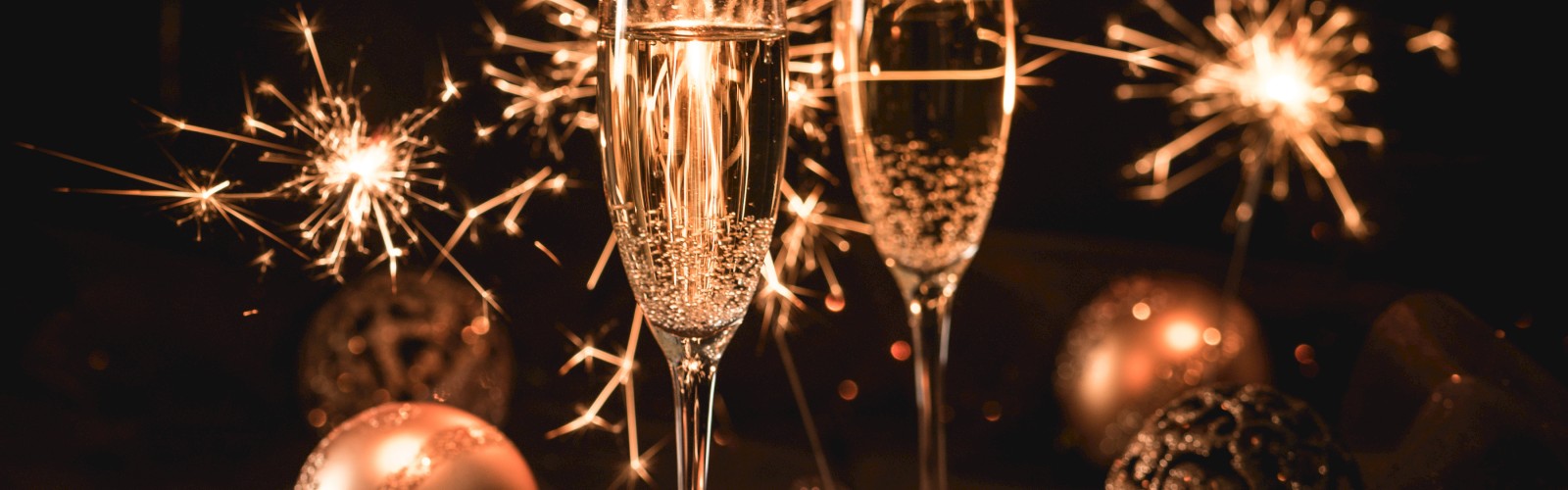 Two champagne glasses with sparklers and baubles in the background, creating a festive atmosphere.