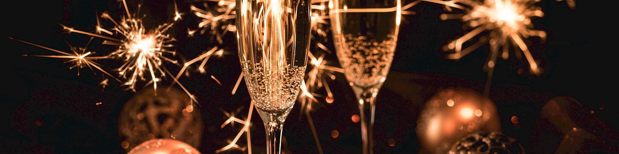 Two champagne glasses with sparklers and baubles in the background, creating a festive atmosphere.