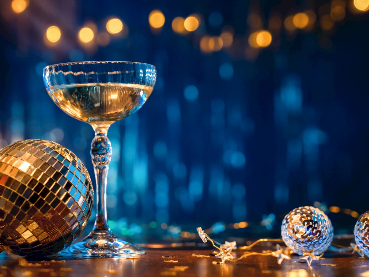 A champagne glass with a disco ball and decorative lights in the background, creating a festive atmosphere.