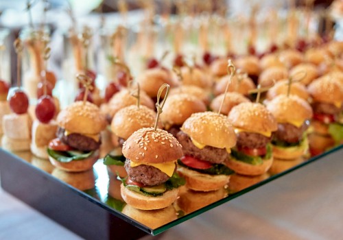 Mini sliders on a tray with sesame buns, toothpicks, and toppings—tiny burgers lined up for a crowd.