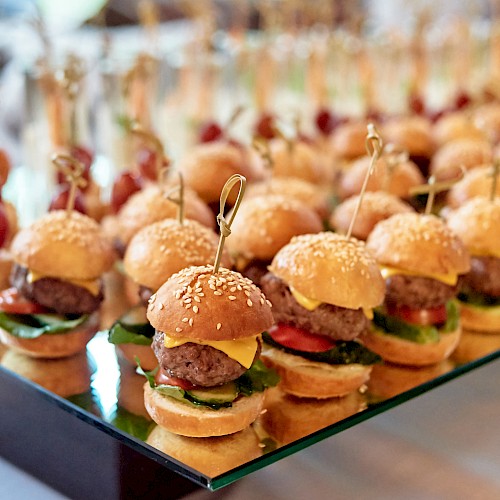Mini sliders on a tray with sesame buns, toothpicks, and toppings—tiny burgers lined up for a crowd.