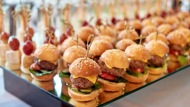 Mini sliders on a tray with sesame buns, toothpicks, and toppings—tiny burgers lined up for a crowd.