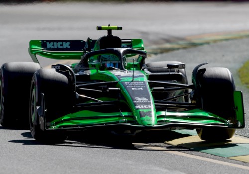 A green and black Formula 1 car is racing on a track, with various sponsor logos visible on its body, including “KICK”.