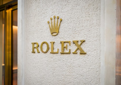 The image shows the Rolex logo on a textured wall, featuring the brand name beneath a crown symbol.