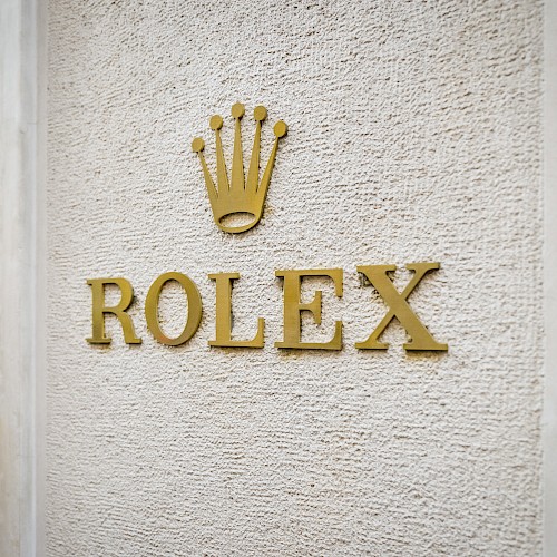 The image shows the Rolex logo on a textured wall, featuring the brand name beneath a crown symbol.