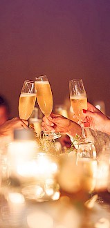 People are raising champagne glasses in a toast, surrounded by a warmly lit, elegant setting with blurred background details.