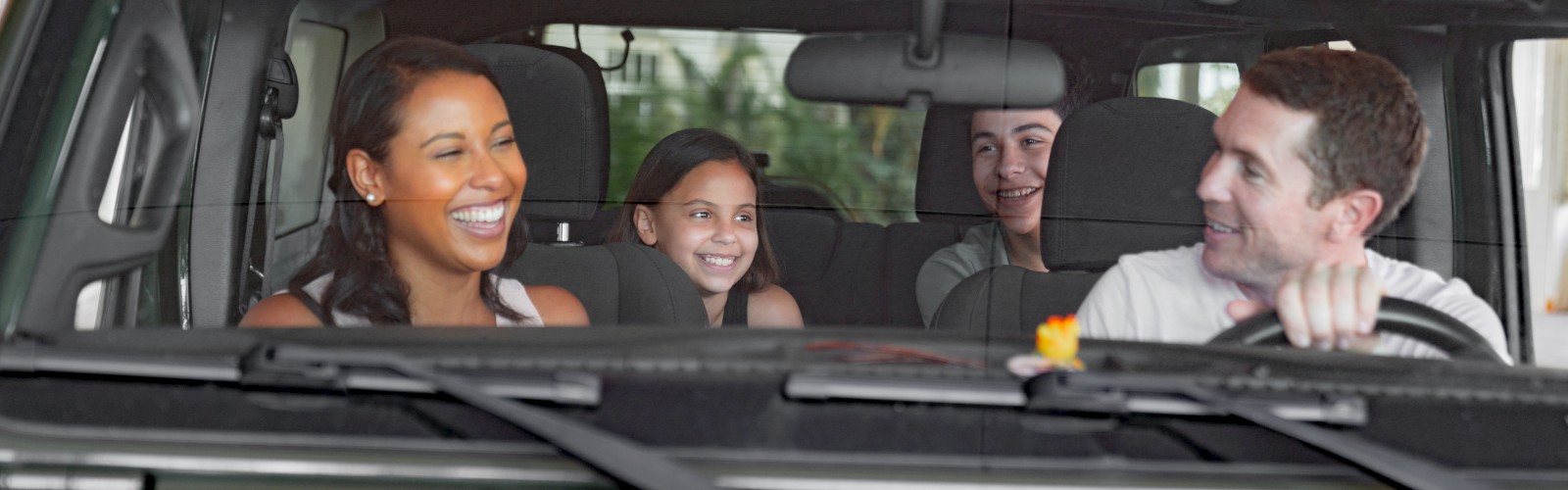 A family of four is sitting in a car, smiling and enjoying their time. The driver is at the wheel, and they seem to be having fun together.
