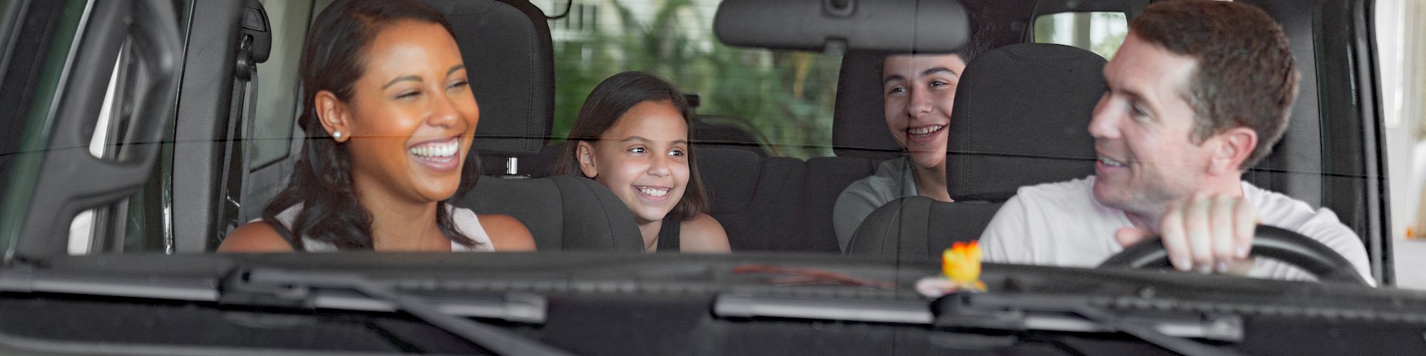 A family of four is sitting in a car, smiling and enjoying their time. The driver is at the wheel, and they seem to be having fun together.