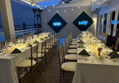 Elegant dining setup with long tables, white tablecloths, and green napkins; neon signs on the wall read 