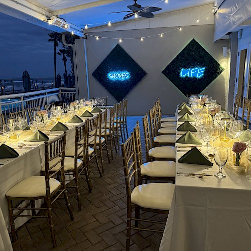 Elegant dining setup with long tables, white tablecloths, and green napkins; neon signs on the wall read 