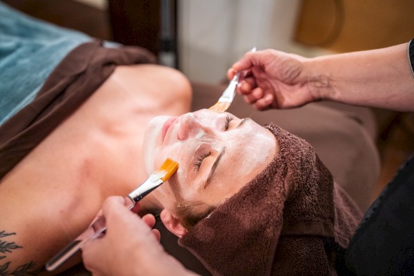 A person is receiving a facial treatment with brushes, lying down with a towel on their head.